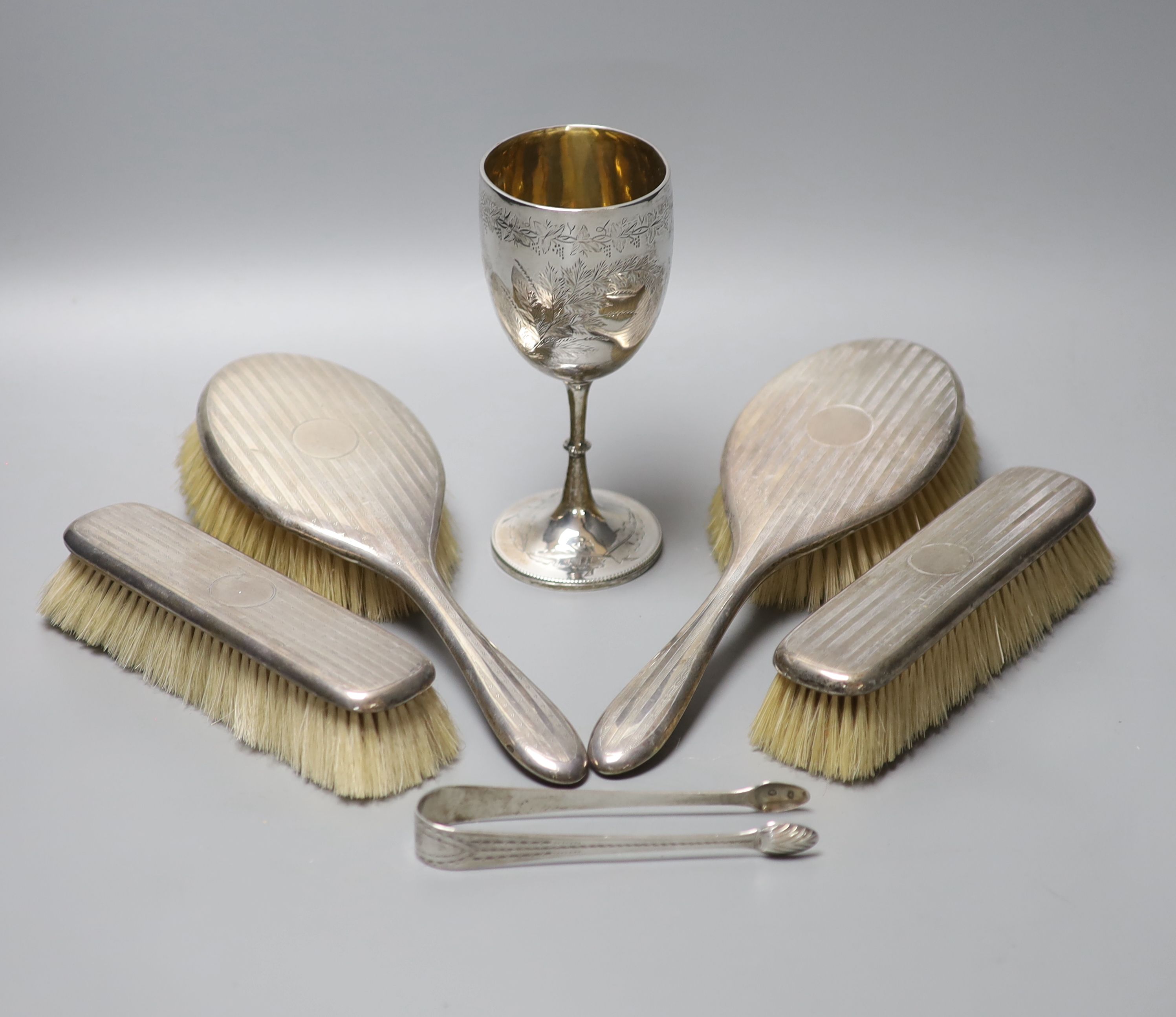 A Victorian engraved silver goblet, London, 1875, 6.3cm, a pair of silver sugar tongs and four silver mounted brushes.